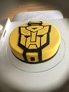 a yellow and black cake sitting on top of a white table next to a cup