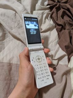 a person holding a cell phone in their hand on top of a bed with sheets