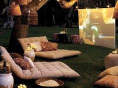 an outdoor lounge set up in the grass with pillows and lights on it's side