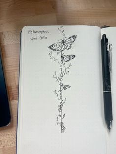 an open notebook with a drawing of butterflies on it next to a cell phone and pen