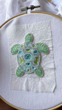 a close up of a cross stitch pattern on a white piece of cloth with a green turtle in the center