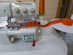 an orange ribbon is being used to sew on a white sewing machine with two buttons