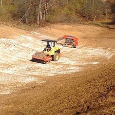 two tractors are driving in the dirt near some trees