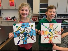 two children holding up paintings in the classroom