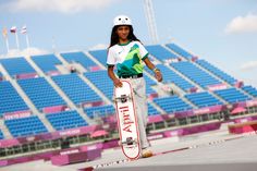 a young woman holding a skateboard in front of a stadium filled with blue seats