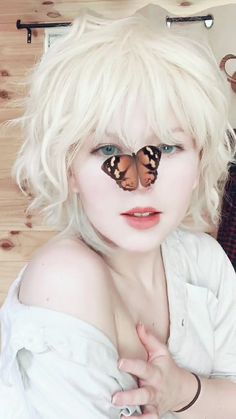 a woman with white hair and butterfly wings on her face is posing for the camera