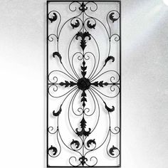 an ornate iron wall hanging on the side of a white wall with light coming through it