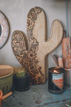 a wooden cactus sitting on top of a table next to potted plants and candles