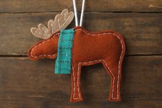 a felt moose ornament hanging on a wooden surface with two strings attached to it