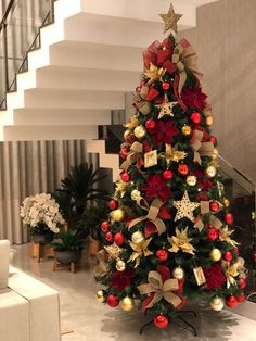 a christmas tree decorated with red, gold and silver ornaments in a living room next to stairs