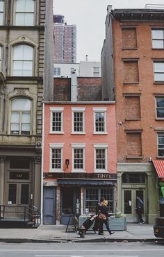 two people walking down the street in front of tall buildings