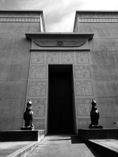 two statues in front of a building with an entry way leading to the entrance area