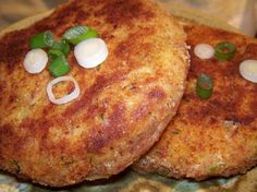 two fried patties with onions and green onions on top are sitting on a plate