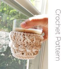 a hand is holding a crocheted cup holder in front of a window sill