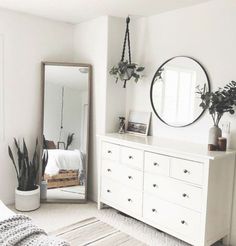 a bedroom with white furniture and plants on the dresser next to a large round mirror