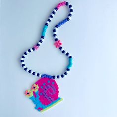 a beaded necklace with a pink and blue object on it's end, sitting on a white surface