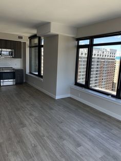 an empty living room with wood floors and large windows overlooking the cityscape outside