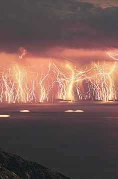 the sky is filled with lots of bright lights as lightning strikes in the distance over water