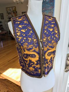 Late 1960s Saint Laurent Rive Gauche Purple and Gold Dragon Vest. This vest is decorated with gold dragons and clouds that are cut out of the purple background. The trim is braided brown cord and wrapped gold metal and is applied to all of the seams as well as center front. The front closes with five buttons that have gold filagree covers. One of the filagree button covers is missing, but otherwise the vest is in excellent condition. Size 34 Bust: 34" Waist: 33" Shoulders: 14" Length: 17.5" Arlington Va, Gold Dragon, Late 1960s, Button Covers, Rive Gauche, Purple Background, Vest Outfits, Purple Backgrounds, The Purple