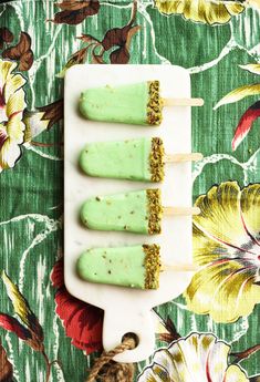 three popsicles with green toppings sitting on a white plate next to a flowered tablecloth