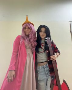 two women dressed in costumes standing next to each other, one holding a guitar and the other wearing a pink wig