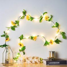 yellow flowers are arranged on the wall next to a book and lantern light garland with green leaves