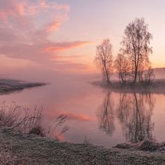 the sun is setting over a lake with some trees in it and fog on the water