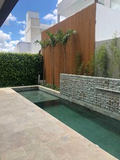 an outdoor swimming pool surrounded by greenery and stone walls with trees in the background