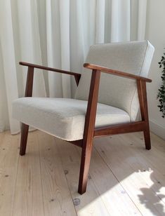 a chair sitting on top of a wooden floor next to a white curtained window