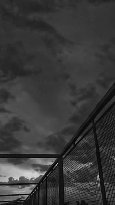 black and white photograph of people walking over a bridge at night with clouds in the background