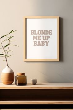 there is a vase with a plant in it next to a framed print that says blonde me up baby