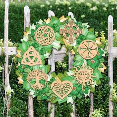 a wreath made out of wooden cutouts sitting on top of a green fence surrounded by bushes