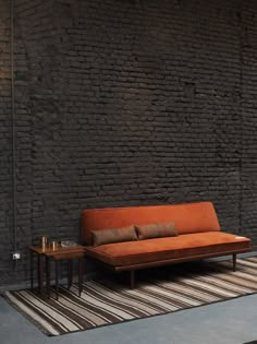 an orange couch sitting on top of a rug next to a table and chair in front of a brick wall