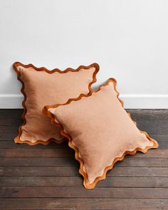 two pillows sitting on top of a wooden floor next to a white wall with a brown scalloped edge