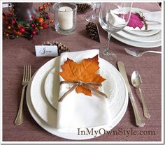 a place setting with an orange leaf on the napkin and silverware, along with pine cones