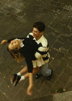 a man and woman are walking down the street holding each other's arms as they laugh