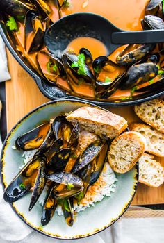 mussels and bread on a plate in front of a skillet filled with sauce