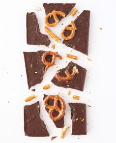 pieces of chocolate with pretzels and nuts scattered around them on a white surface