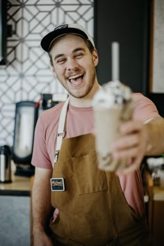 a man in an apron is smiling and holding a cup with ice cream on it