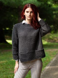 a woman with red hair is standing in the grass wearing plaid pants and a black sweater