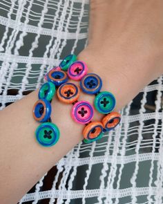 a woman's arm with colorful bracelets on top of it and buttons attached to the wrist