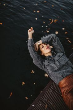 a woman standing next to a body of water holding her hands up in the air