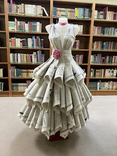 a dress made out of newspapers sitting in front of a book shelf filled with books