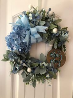 a baby boy wreath with blue flowers and greenery hanging on the front door,