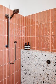 an orange tiled bathroom with shower head and soap dispenser