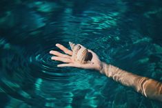 a person's hand reaching for a seashell in the blue water with ripples