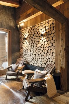 two chairs and a table in front of a wall made out of logs with lights on them