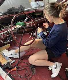 a woman sitting on the floor working on a car's steering wheel and wires