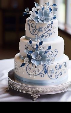 a three tiered wedding cake with blue flowers on the top and bottom, sitting on a silver platter