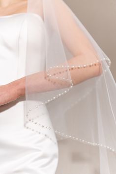 a woman in a white wedding dress with a veil on her head and beaded wrist